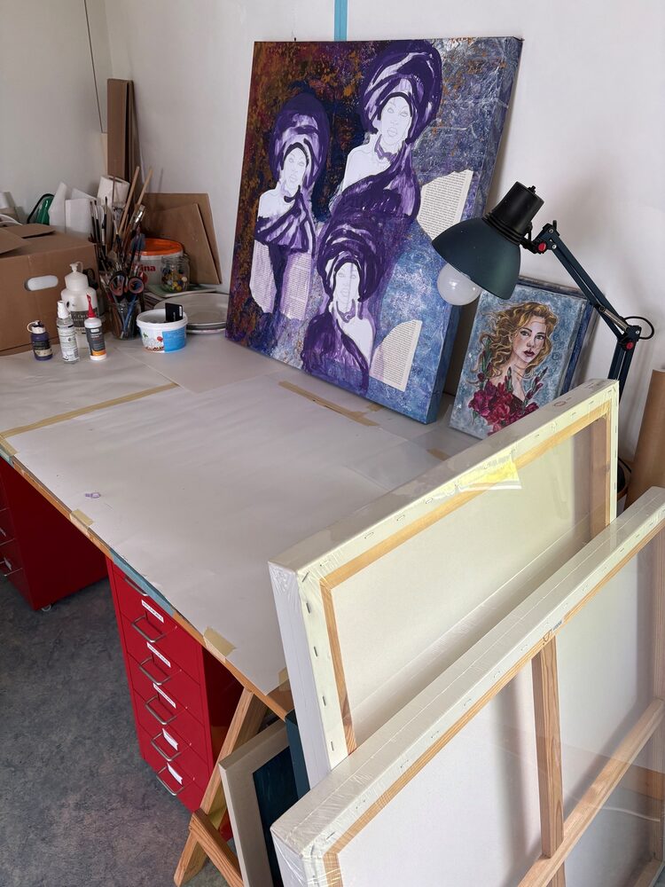 Carolyn's small studio: worktable with a large purple and silver painting in progress, paints, brushes, a red drawer cabinet and stacked canvases